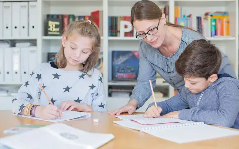 Lehrerin hilft zwei Schülern bei der Nachhilfe Realschule. Sie schreiben konzentriert in ihre Hefte.