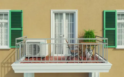 Balkon eines Mehrfamilienhauses mit Klimaanlage, Tisch und Stuhl. Grüne Fensterläden und eine Tür mit Vorhängen.