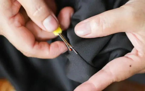 Hands use a seam ripper to open a pocket on black fabric. This is how suit pockets are sewn shut to maintain their shape during shipping.