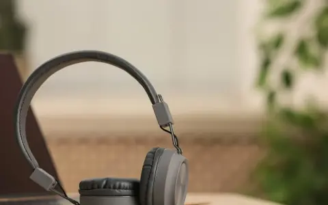 Szare słuchawki dynamiczne na drewnianym blacie, obok laptopa. Idealne do słuchania muzyki i podcastów.