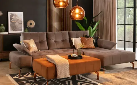 Elegancki salon z sofą w kolorze taupe. Idealnie komponuje się z pomarańczowym pufem, miedzianymi lampami i złotymi dodatkami.