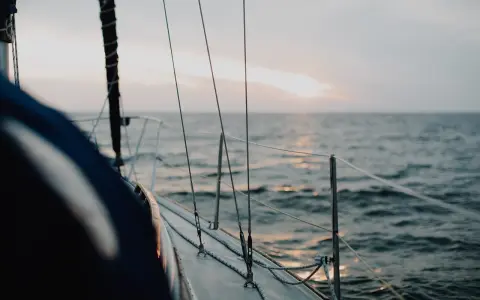 Vue depuis le pont d'un voilier insubmersible naviguant sur une mer calme au coucher du soleil.