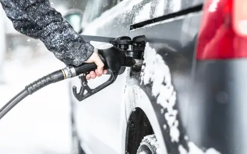 Ręka w zimowej kurtce trzyma pistolet do tankowania, nalewając diesel paliwo do samochodu podczas opadów śniegu.