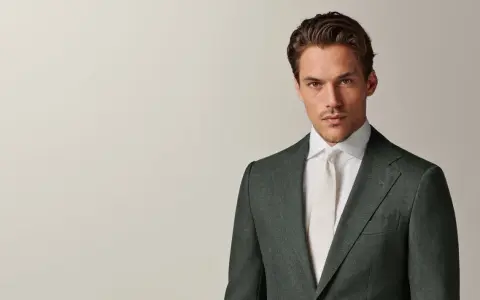A man in a dark green suit and white shirt with a cream tie. This timeless look embodies the perennial suit meaning of enduring style and sophistication.
