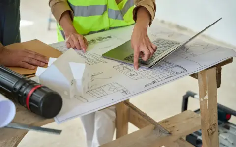 Architectes discutent des plans, pointant du doigt l'emplacement idéal pour installer la VMC dans le modèle de maison.