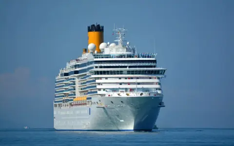 La nave da crociera Costa Luminosa solca il mare calmo sotto un cielo azzurro.