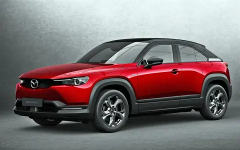 Czerwona Mazda MX-30 z czarnym dachem prezentuje się stylowo na tle szarej ściany.