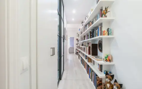 Pasillos estrechos y modernos con estanterías blancas repletas de libros y objetos decorativos, creando un ambiente acogedor.