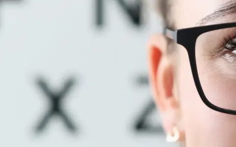 Kiedy dobrać okulary po operacji zaćmy? Zbliżenie na oko w okularach, na tle tablicy Snellena.