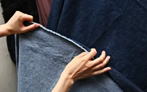 Dłonie dotykają ciemnoniebieskiego denimu i szarej tkaniny, być może z domieszką elastanu, sprawdzając ich fakturę.