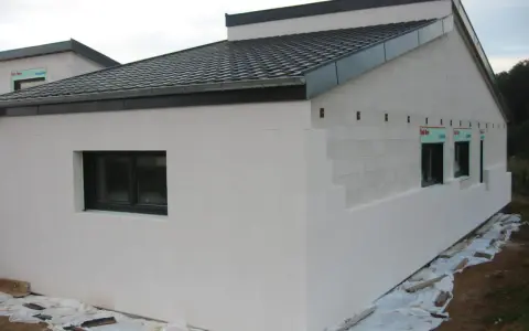 Maison en construction avec murs en **béton cellulaire extérieur**. Fenêtres noires et toit sombre.