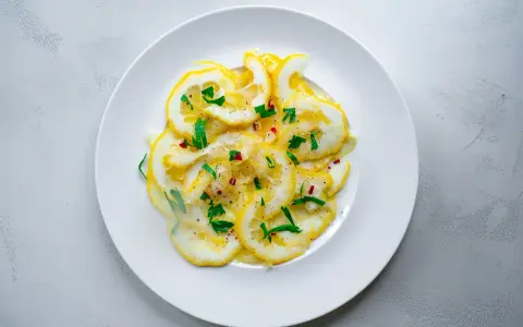 Dünne Scheiben Zitrone mit Zucker bestreut, garniert mit frischen Kräutern und Chiliflocken. Ein erfrischender Genuss!