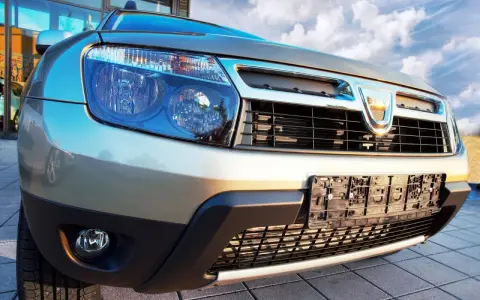 Złoty Dacia Duster 1.6 benzyna z bliska, z widocznym grillem, reflektorami i tablicą rejestracyjną.