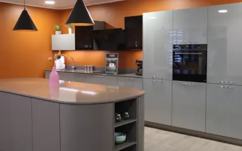 Cuisine moderne avec îlot central et armoires grises. Les murs orange vif contrastent avec les surfaces épurées, créant une ambiance chaleureuse. Une cuisine sans hotte, mais avec un design élégant.