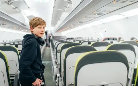 Chłopiec z słuchawkami na szyi w pustym samolocie. Zastanawia się, od ilu lat można latać samemu.