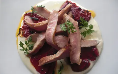 Lonchas de cerdo tierno sobre una cama de puré cremoso y pimiento del piquillo asado, decorado con perejil fresco.