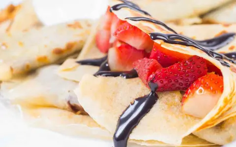 Deliziose crepes senza burro, ripiene di fragole fresche e ricoperte da una golosa salsa al cioccolato.