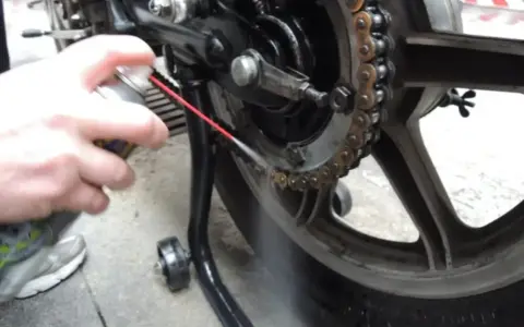Mano spruzza lubrificante sulla catena della moto. Per sapere ogni quanto ingrassare catena moto, controlla il manuale.