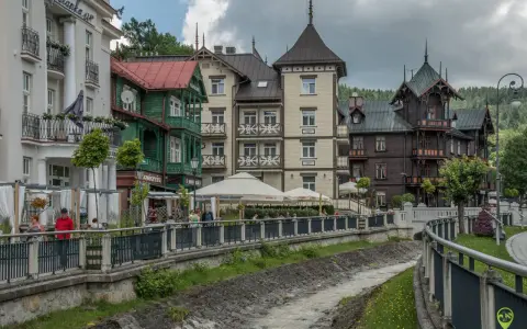 Krynica-Zdrój latem: malownicza promenada nad potokiem, zabytkowe wille i kawiarniane ogródki.
