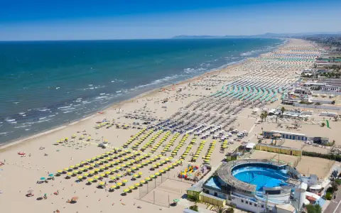 Słoneczna plaża w Rimini, pełna leżaków i parasoli, zaprasza na wakacje. Idealne miejsce na loty do Rimini!