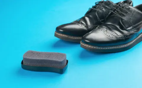 Czarne buty ze sztucznej skóry i gąbka do pastowania. Czy można pastować buty ze sztucznej skóry? Tak, specjalnymi preparatami.
