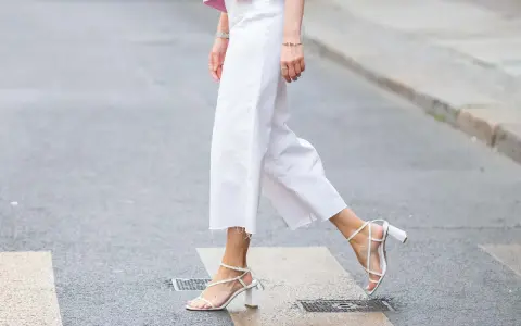 Mujer cruza la calle con un look comunión: pantalón blanco de corte ancho y sandalias de tiras.