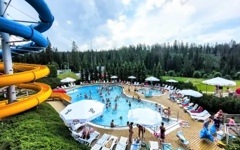Aqua park Bukowina tętni życiem. Ludzie kąpią się w basenie, zjeżdżają ze zjeżdżalni i odpoczywają na leżakach.