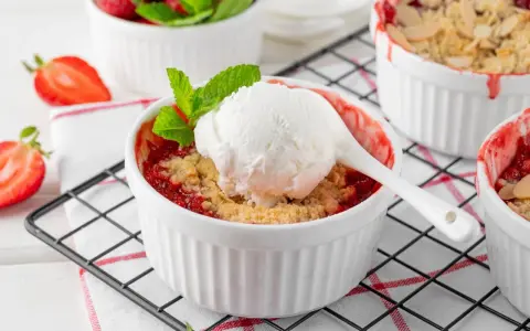 Pyszny crumble z truskawkami w białych kokilkach, ozdobiony świeżymi owocami i miętą.