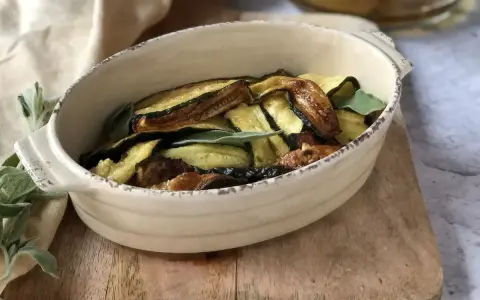 Zucchine in carpione dorate e saporite, guarnite con foglie di salvia fresca, servite in una ciotola rustica.