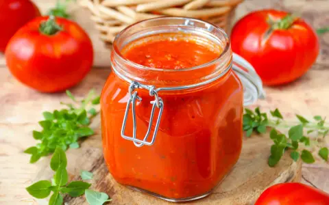 Un bocal de sauce tomate maison, avec des tomates fraîches et du basilic disposés autour.