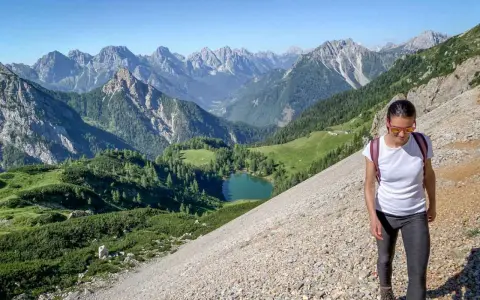 Una donna fa una camminata outdoor in montagna, godendosi il panorama di un lago alpino e vette maestose. Il vero significato di camminata outdoor è qui.