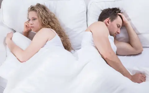 Para, odwróceni do siebie plecami w łóżku, zmartwiona kobieta i mężczyzna z ręką na czole. Czy to pochwica? Co to za problem?