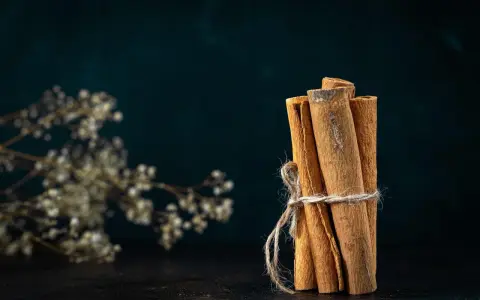 Pęczek lasek cynamonu, związany sznurkiem, obok delikatnych, suchych kwiatów. Cynamon właściwości magiczne, zapach unoszący się w powietrzu.