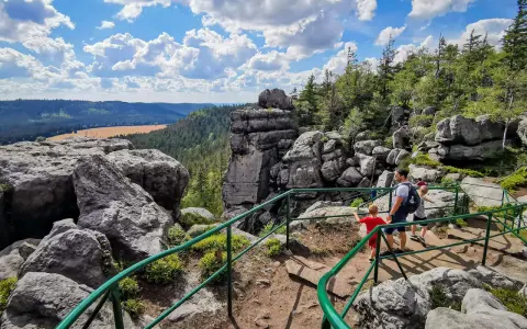 Rodzina wędruje po skalistej trasie Szczeliniec Wielki. Widok na dolinę i chmury.