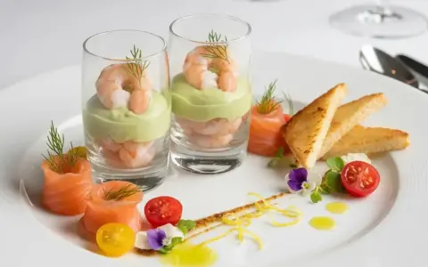 Recette entrée froide gastronomique facile : crevettes et avocat en verrine, saumon fumé roulé, toasts grillés, tomates cerises et fleurs comestibles.