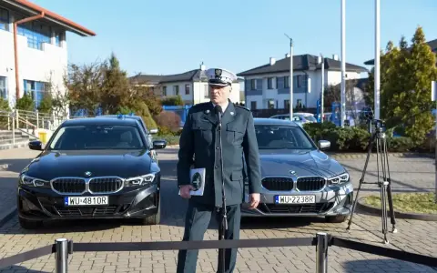 Funkcjonariusz w mundurze stoi między dwoma nieoznakowanymi radiowozami BMW.