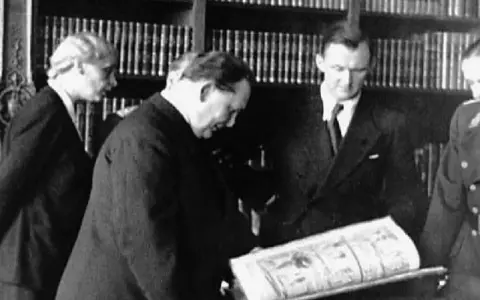 Bruno Lohse et d'autres hommes examinant un livre ouvert dans une bibliothèque.