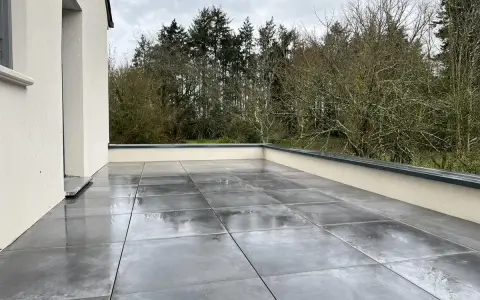 Terrasse avec dalles grises sur un toit plat, offrant une vue sur une forêt. L'étanchéité du toit plat est assurée pour une durabilité optimale.