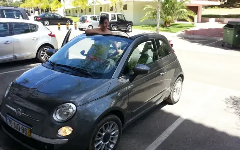 Frau lehnt sich aus einem grauen Fiat 500 Cabrio, bereit für eine Spritztour. Hier sind einige mietwagen portugal tipps für Ihren Urlaub!