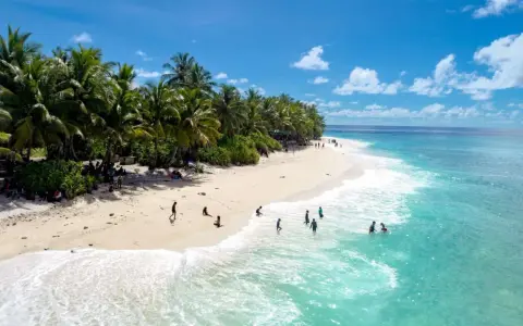 Spiaggia tropicale con palme e persone che nuotano nell'acqua cristallina dell'atollo di Maafushi.
