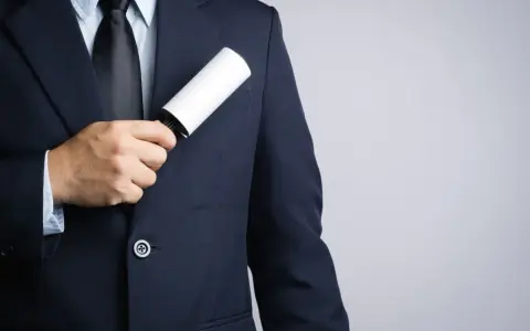 A man in a dark tuxedo uses a lint roller to clean his jacket, showing a simple way how to clean a tuxedo.