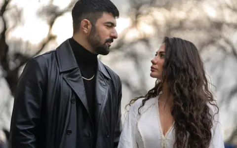 Un uomo con trench di pelle nera e una donna con lunghi capelli scuri si guardano intensamente. Io sono Farah, e questo sguardo dice tutto.