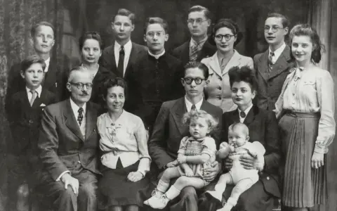 Gros plan sur une famille nombreuse posant pour une photo. On peut y voir des enfants, des adultes et des bébés. Une recherche sur Geneanet pourrait révéler leur nom de famille.