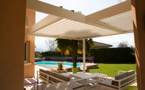 Une pergola bioclimatique moderne avec des lames orientables protège un salon extérieur et une piscine.