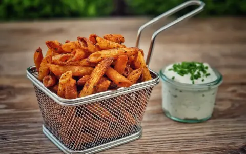 Knusprige Nudel-Chips in einem Metallkorb, daneben ein Glas Dip mit Schnittlauch.