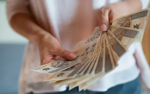 Dłonie trzymają wachlarz polskich banknotów. Zastanawiasz się, czy nagroda jubileuszowa wlicza się do emerytury?
