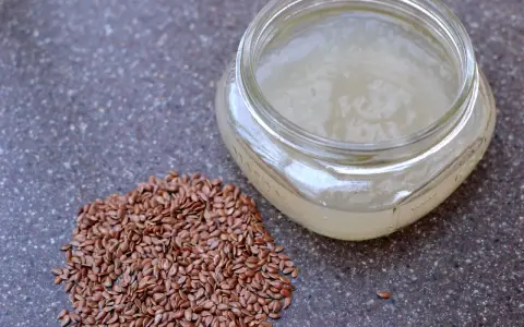 Graine de lin pour rajeunir : une poignée de graines de lin brunes à côté d'un pot en verre rempli d'un gel clair, peut-être un sérum fait maison.