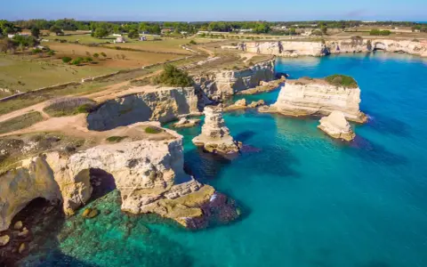 Scogliere bianche e mare turchese in una splendida **Puglia estate**. Faraglioni emergono dall'acqua cristallina, un vero paradiso.