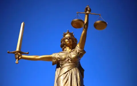 Statua dorata della Giustizia con spada e bilancia, simbolo dei giudici ordinari, contro un cielo blu intenso.