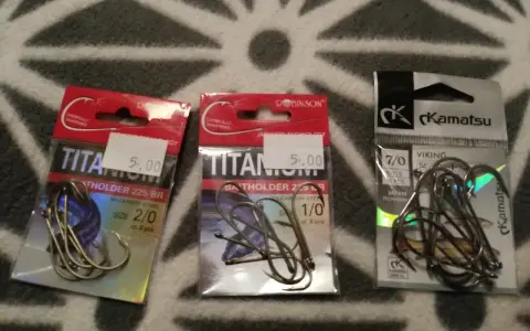 Trzy opakowania haczyków wędkarskich. Dwa z napisem "TITANIUM" i jeden z logo "Kamatsu". Idealny haczyk na lina czeka!